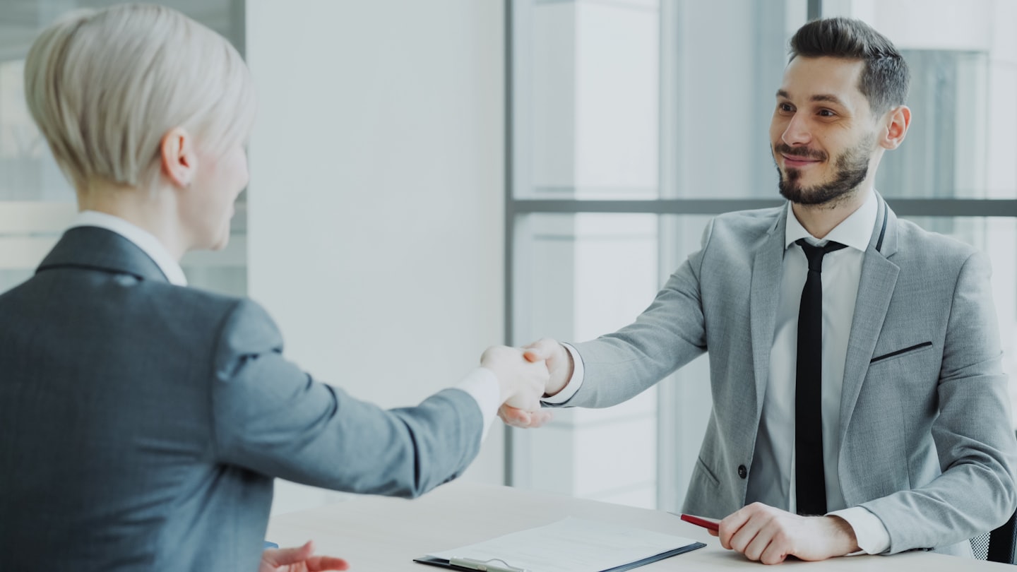 Two business professionals shaking hands over a desk.